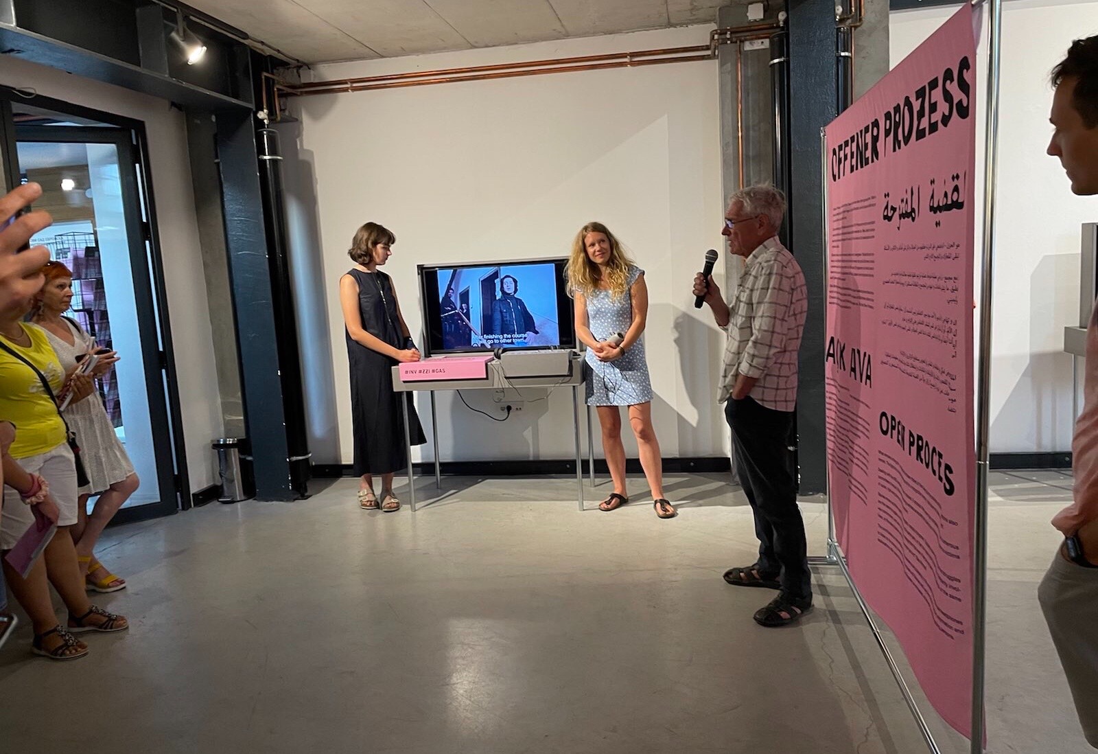 Der Filmemacher Želimir Žilnik spricht bei der Eröffnung der Ausstellung "Offener Prozess". Im Hintergrund läuft sein Kurzfilm "Inventur - Metzstraße 11" über das Leben der sogenannten Gastarbeiter*innen, der in der Ausstellung zu sehen ist.