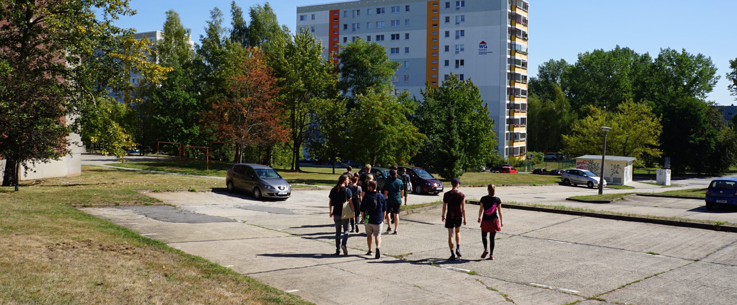 Eine Gruppe von Menschen geht in Richtung eines Plattenbaus im Fritz-Heckert Gebiet.