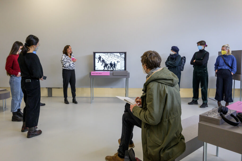 Personen, die während einer Vermittlungsrunde ein Video in der Ausstellung ansehen